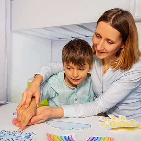 Boy with autism learn weather using cards, teacher hold hands and point to correct one